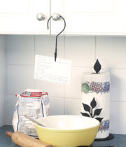 Cabinet-mounted hanger holder for recipe cards in a kitchen setup, keeping instructions visible above a mixing bowl and baking tools.