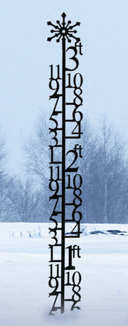 Tall 3 Foot Snowflake Snow Gauge standing in snow-covered yard, featuring large numeric markers for precise snowfall measurement.