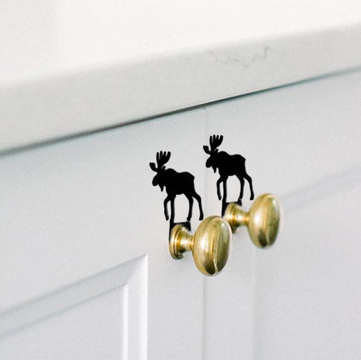 Moose silhouette cabinet knob accents on white cabinet doors, adding a playful rustic touch to kitchen hardware.