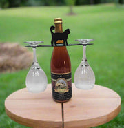Outdoor display of Cat Wine Caddy wine rack featuring black cat design, securely holding a wine bottle and two glasses on a wooden table.