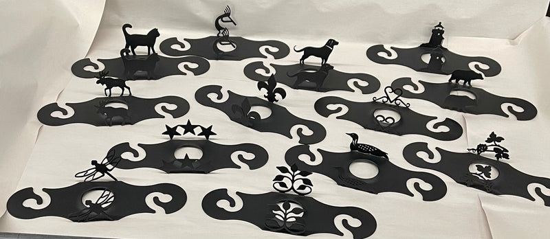 Assorted Wine Caddy Closeout designs in black metal with various decorative cutouts, perfect for wine bottle holders in kitchen and dining decor.