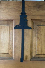 Black metal Lighthouse Door Wreath Hanger on a wooden door, ideal for hanging seasonal wreaths in coastal-themed home decor.