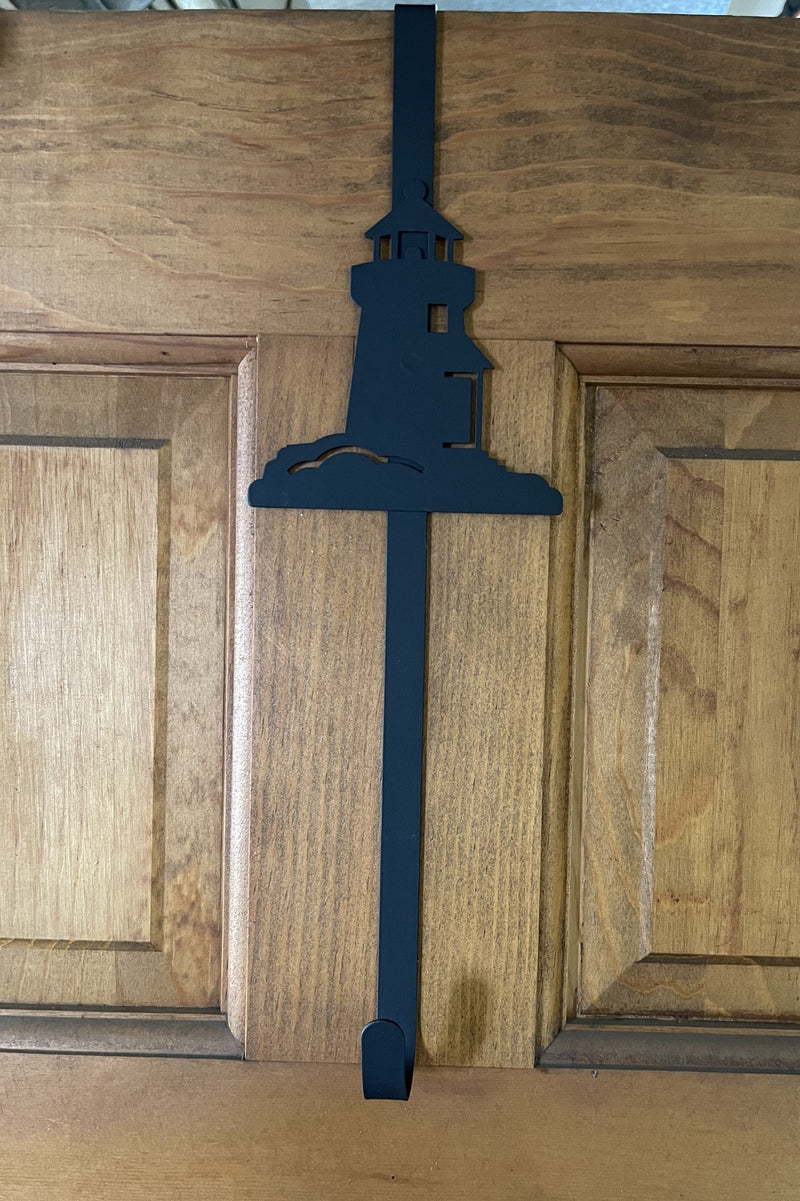 Black metal Lighthouse Door Wreath Hanger on a wooden door, ideal for hanging seasonal wreaths in coastal-themed home decor.